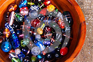 Colorful glass beads of various shapes and sizes placed inside a wooden bowl