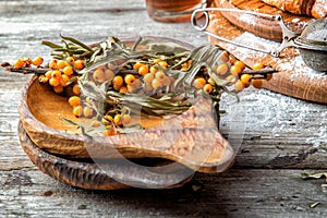 Close up. Wooden bowl with sprigs of bright yellow sea buckthorn berries. Rustic wooden background