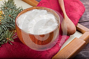 Close-up wooden bowl with yogurt, spoon and fir twig on red napkin  on wooden table.
