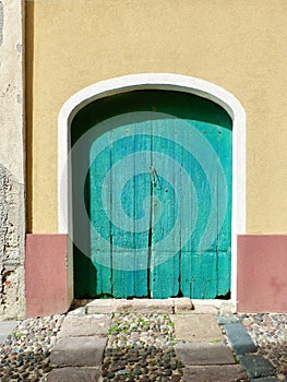 Close up wooden closed door of old barn on painted wall on the streets of Alghero, Sardinia, Italy. Vintage Italian architecture