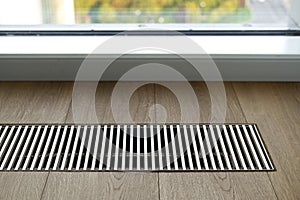 Close up of wooden floor with chrome ventilation grid of central heating against window