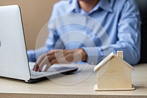 Close up wooden House model, Businessman using laptop. housing purchase, Property, real estate and insurance concepts