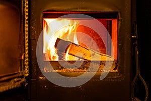 Close up of wooden logs burning in wood burning fire with open door in home living room.