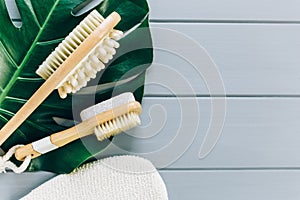 Close up Wooden massage brushes for skin and body care and monstera tropic leaf on gray background. Beauty, spa and bath concept.