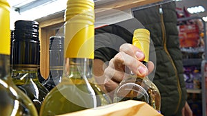 Close-up of a wooden rack with various bottles of wine and a male buyer\'s hand takes one