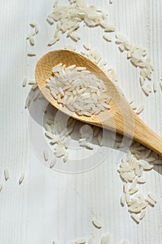 Close-up of wooden spoon with raw white rice, on white wooden table, horizonta