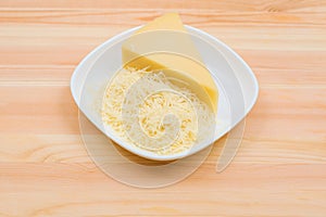 Close-up on a wooden table in a plate is Parmesan cheese in grated and brick form. The concept of solid dairy products