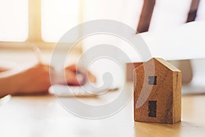 Close up wooden toy house with hand signing loan document to home ownership