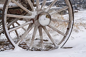 Close up of the wooden wheel of an old wagon against a snowy terrain in winter