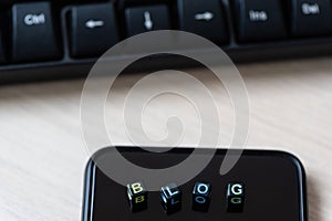 Close up words BLOG on blocks on black smart phone on desk