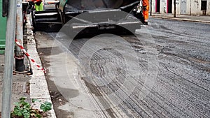Close up of the work of an asphalt paver. Hot asphalt, bitumen. Asphalt paver bunker for road repair. Road repair in the