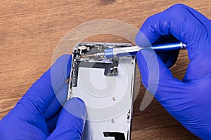 Close-up on the work of unscrewing the faulty part of the smartphone, by the hands of a master in blue gloves