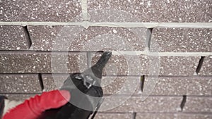 Close-up of a worker fills a joint between bricks with mortar from a sealant gun. The master evens out the seams between