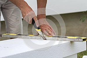 Close-up of worker hand with knife and level cutting white rigid