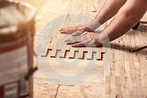 Close up of worker installing wood parquet. Carpenter on work putting wood parquet pieces