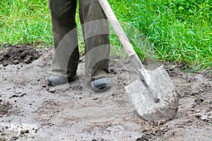 Close up of worker man legs digging soil, ground with shovel in rubber boots in garden