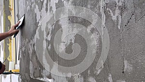 Close-up of a worker's hand with a trowel applying mortar to white mesh and rigid polyurethane foam for home