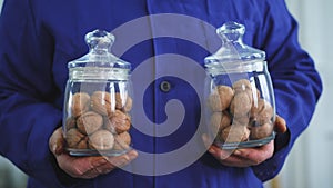 Close-up, worker s hands hold two glass jars of walnut, of different kinds, grown selectively, hybrids of nuts of better