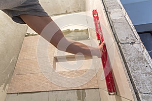 Close-up of worker tiler hand with lever installing on walls ceramic tiles. Tiles installation, tools and home improvement,