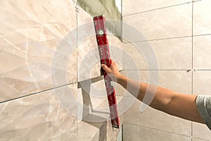 Close-up of worker tiler hand with lever installing on walls ceramic tiles. Tiles installation, tools and home improvement,