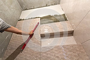 Close-up of worker tiler hand with lever installing on walls ceramic tiles. Tiles installation, tools and home improvement,