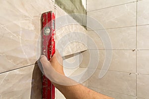 Close-up of worker tiler hand with lever installing on walls ceramic tiles. Tiles installation, tools and home improvement,