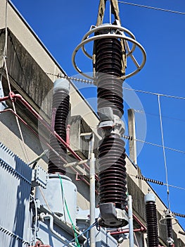 A close-up of a worker using a crane to install a large, ceramic electrical insulator on a high-voltage power transformer.