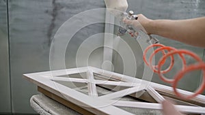 Close-up of a workers hand using a spray gun and painting wood. Painting table on white color. Painting with spray