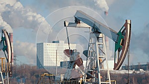 Close-up of a working pump for the extraction of crude oil and of a petrochemical plant`s pipes emissions