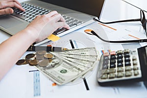 Close up of working woman hand using laptop computer on office desk with money report paper eyeglasses and calculator. Business