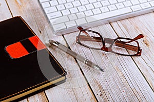 Close up workplace office desk table, reading eye glasses on wooden table with other office stuffs keyboard, notebook and pen