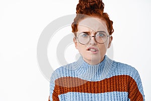 Close up of worried and troubled redhead woman in glasses, frowning and biting lip puzzled, have proble, staring