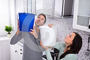 Couple Collecting Water Leaking From Ceiling In Bucket