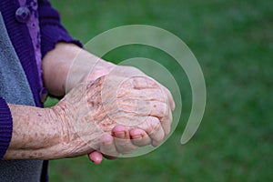 Close-up of wrinkled hands senior woman joined together while standing outdoors. Concept of aged people and healthcare