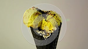 Close-up yellow balls of ice cream in chocolate waffle cup have sprinkling with dry chocolate topping and chopped nuts
