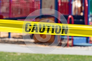 Close-up of yellow cordon tape with word caution, with public park in background