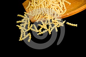 Close up yellow dry uncooked raw Fusilli pasta noodle on wooden board black background