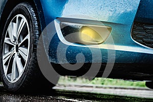 Close up of yellow fog lights on blue car in rainy day.