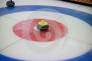 A close-up of a yellow-handled curling stone sits on ice in the center of the House