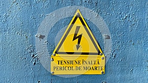 Close-up of yellow high voltage sign on blue door.