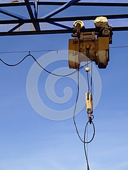 Close up of yellow industrial crane hook (winch) towards blue clear sky. Iron, metal structure. Noblessner
