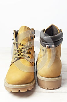 Close-up Yellow men`s work boots from natural nubuck leather on wooden white background. Trendy casual footwear youth style.