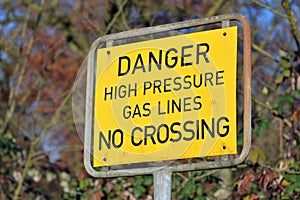 Close up of a yellow outdoor warning sign saying dager high pressure gas line no crossing photo