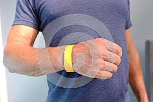 Close-up of yellow paper bracelet, check tape with entry number on hand of middle-aged european man, event ticket concept