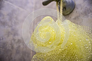 Close-up of a yellow shower puff sponge mesh net ball hanging from a lever handle.