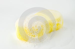 Close up of yellow sponge with soapsuds and bubbles on white background