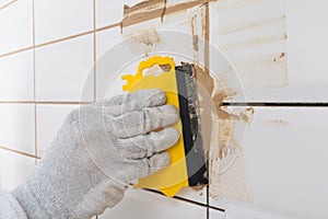 Close-up of a yellow trowel, in the process of grout of a white tile, with a light brown sealant