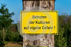 Close-up of a yellow warning sign with German text `Entering the crops at your own risk`