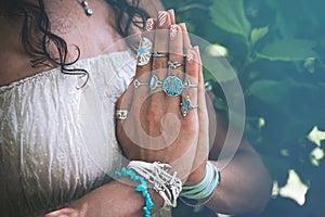 close up of yoga woman hands in namaste gesture with lot of boho style jewelry rings and bracelets outdoor