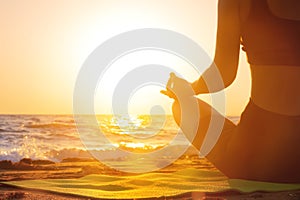 Close-up Yoga woman meditating at serene sunset or sunrise on the beach. The girl relaxes in the lotus position. Fingers